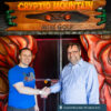 Two men stand outside of the enterance to Cryptid Mountain Miniature Golf shaking hands.