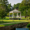 A gezebo sits in the middle of Berkeley Springs State Park. It is sunny and surrounded by trees and lights.