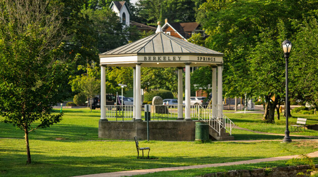 A gezebo sits in the middle of Berkeley Springs State Park. It is sunny and surrounded by trees and lights.