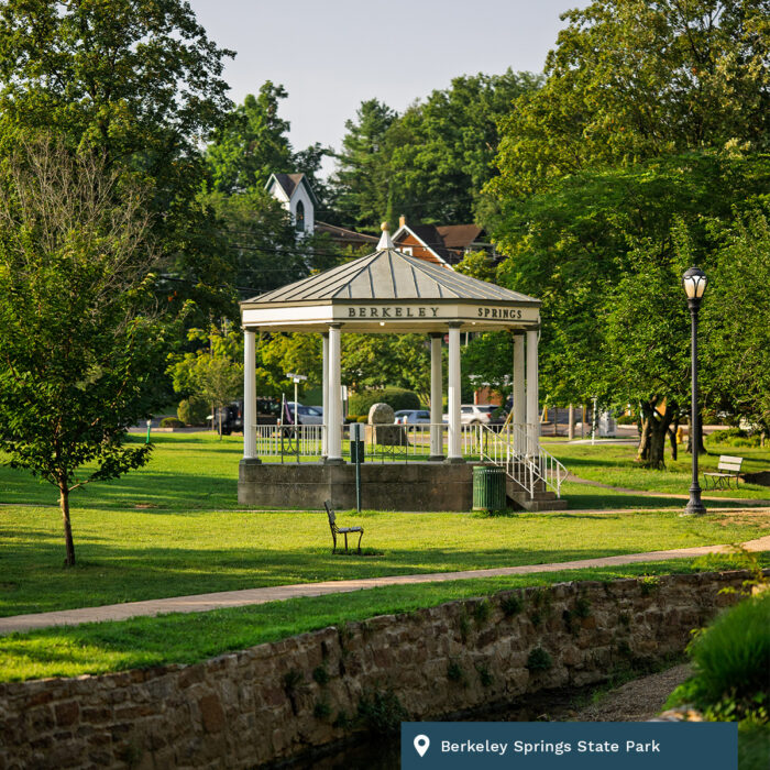 A gezebo sits in the middle of Berkeley Springs State Park. It is sunny and surrounded by trees and lights.