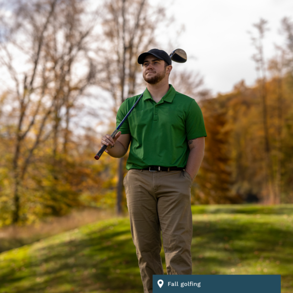 A golfer in a green shirt holds his club in the fall.