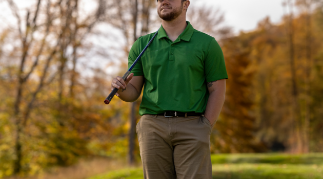 A golfer in a green shirt holds his club in the fall.